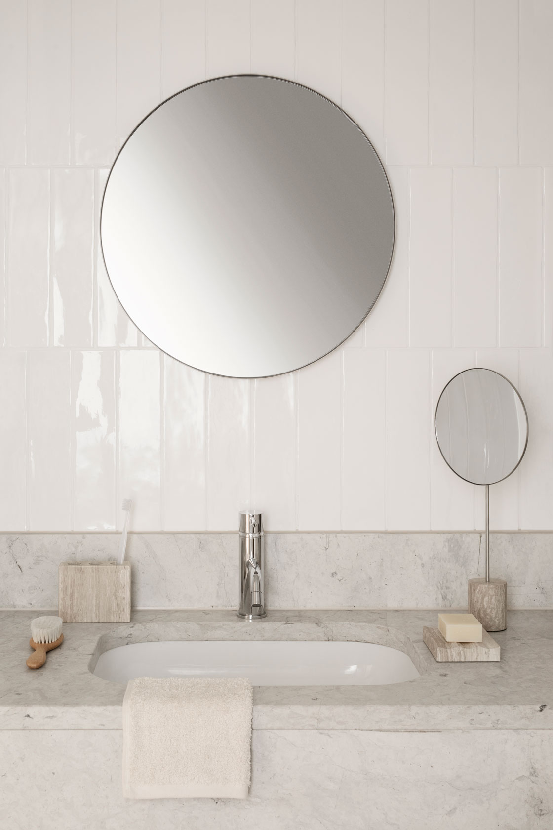 a bathroom sink with a large round mirror in the middle and various marble products surrounding the sink. ( vanity mirror, toothbrush holder, soap holder)