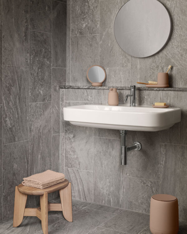 a bathroom setting showing the sink and mirror side with a wooden stool on the side with towels