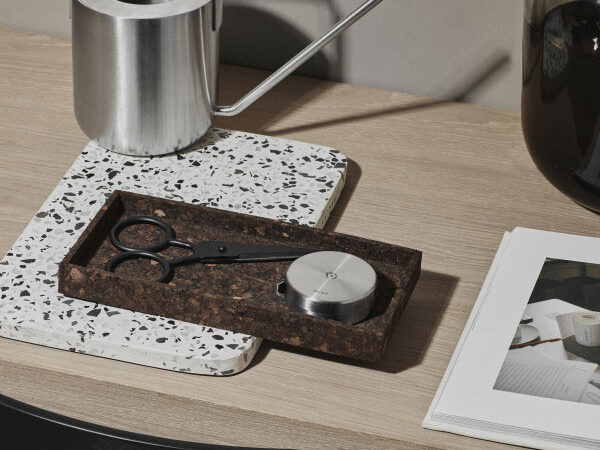 a watering can on a desk alongside with marble terrazzo trays in white and brown colour.