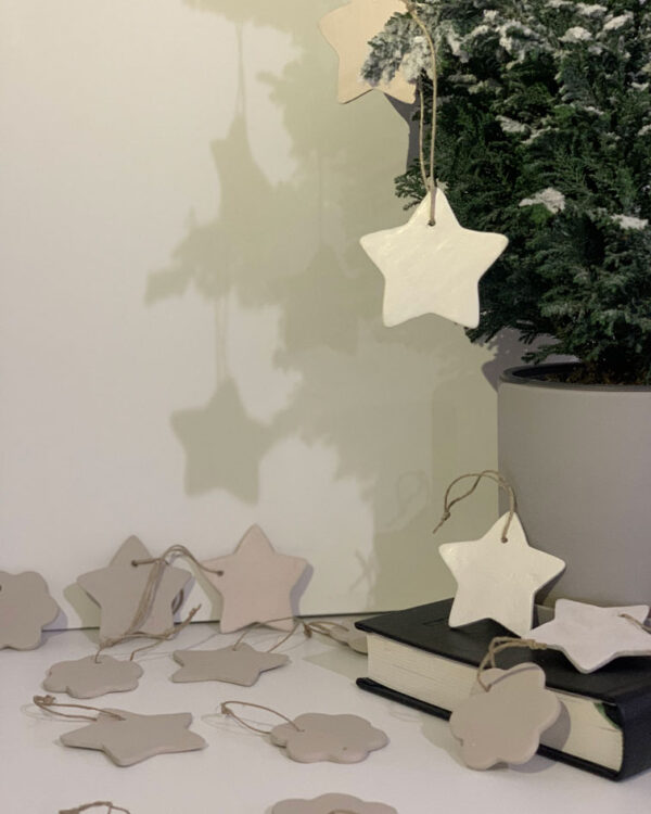 clay ornaments in white hanging from a small tree. shaped as a star and a daisy