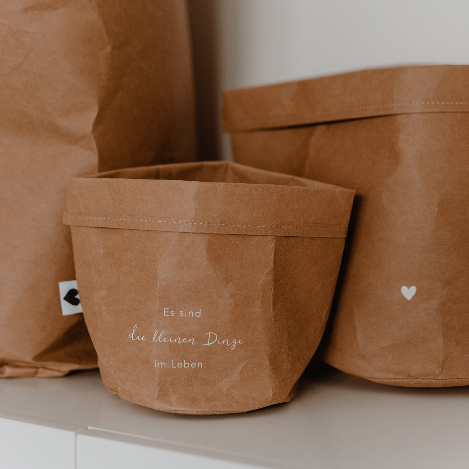 paper baskets in black colour. This set consists of two paper bags in different sizes. The larger paperbag is decorated with a heart. The smaller one bears the saying "It's the little things in life" in German.