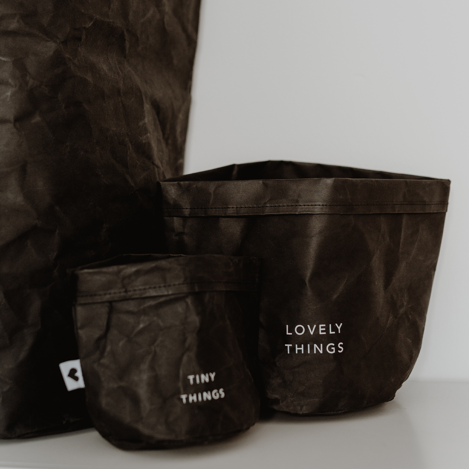 paper baskets in black colour. This set consists of two paper bags in different sizes. The larger paperbag bears the slogan "Lovely Things". The smaller paper bag "Tiny Things".
