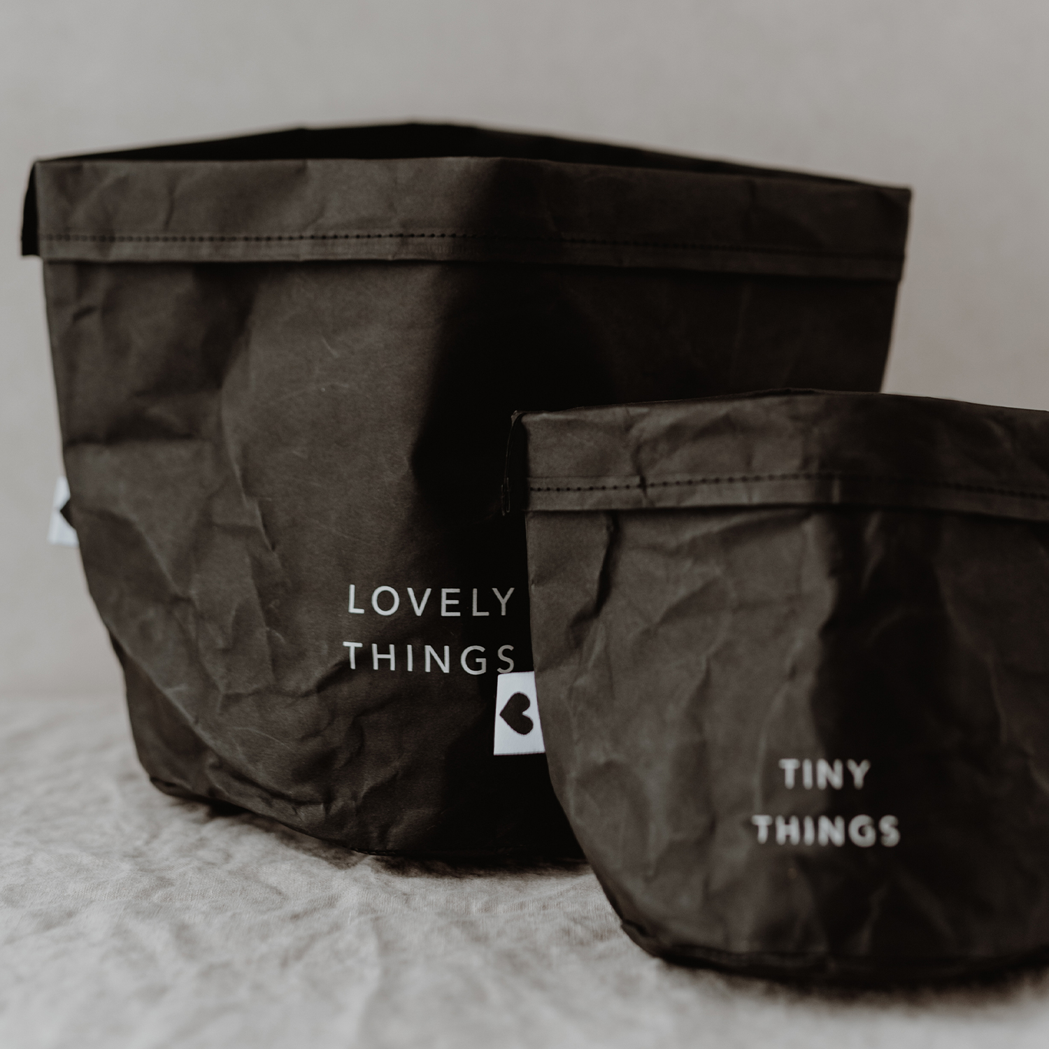 paper baskets in black colour. This set consists of two paper bags in different sizes. The larger paperbag bears the slogan "Lovely Things". The smaller paper bag "Tiny Things".