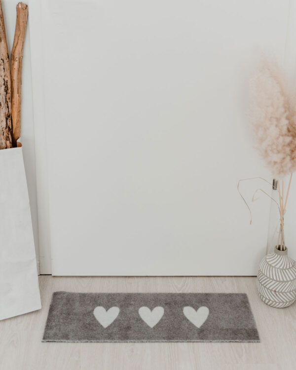 a grey doormat with 3 white hearts on it. 75cm x 25cm.