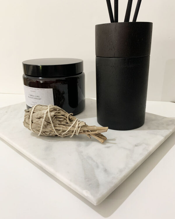 White marble board with a candle a diffuser and sage on it