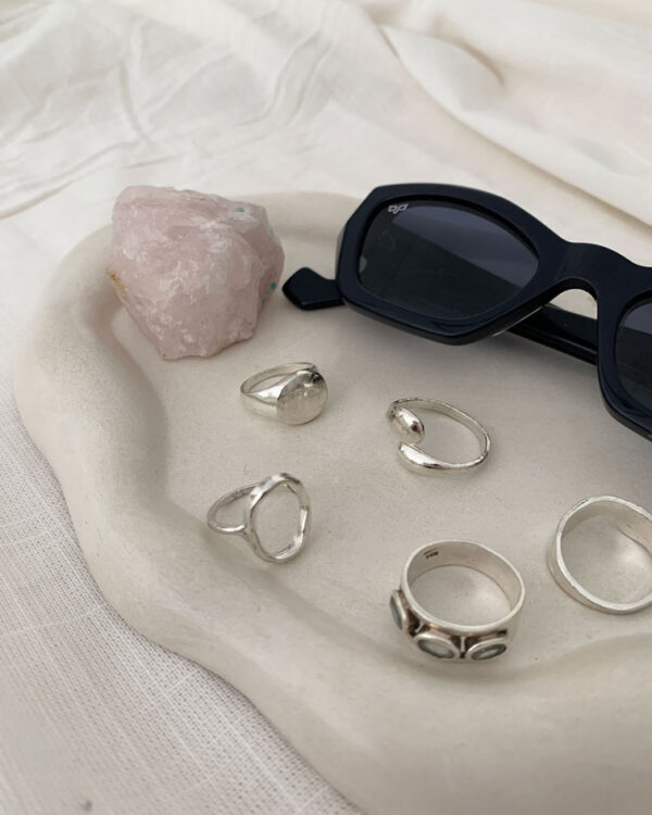 irregular-shaped cloud trays in greige color, with a cloud-like effect on the edges. The trays are made of non-toxic resin, sealed with a natural wax sealer, and have small cork feet to protect furniture. Available in two shapes, oval and round, with unique color variations and air bubbles that add to their contemporary charm. These trays are perfect for decorative use and can be styled in various ways, such as displaying perfumes, candles, or diffusers.