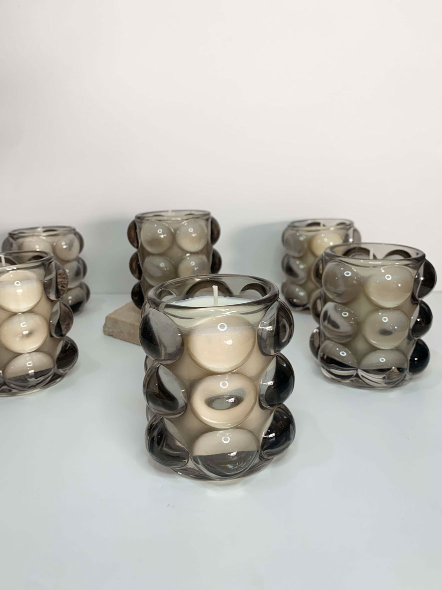Image of multiple scented candles in a bubble glass vessel, emitting a warm glow. Each candle has a unique scent and is labeled with its corresponding fragrance. The glass vessel adds a touch of elegance to the overall presentation