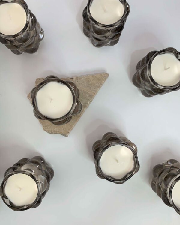 Image of multiple scented candles in a bubble glass vessel, emitting a warm glow. Each candle has a unique scent and is labeled with its corresponding fragrance. The glass vessel adds a touch of elegance to the overall presentation