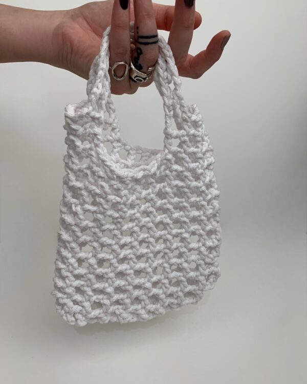 Close-up of a beautiful white crochet bag with a mesmerizing mesh pattern. The intricate design adds elegance and sophistication to any outfit. Perfect for a stylish and chic look.