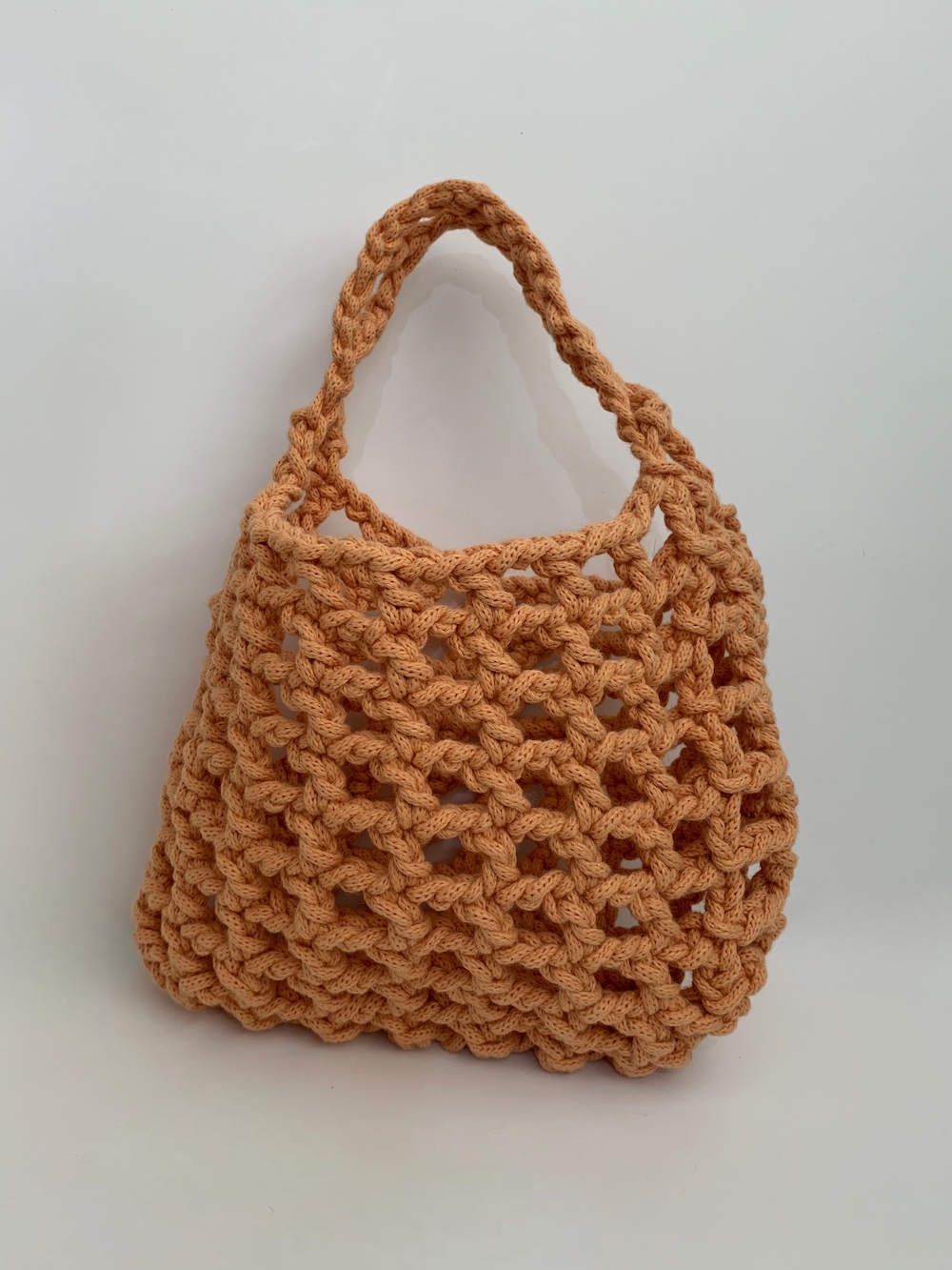 Close-up of a beautiful orange crochet bag with a mesmerising mesh pattern. Perfect for a stylish and chic look.