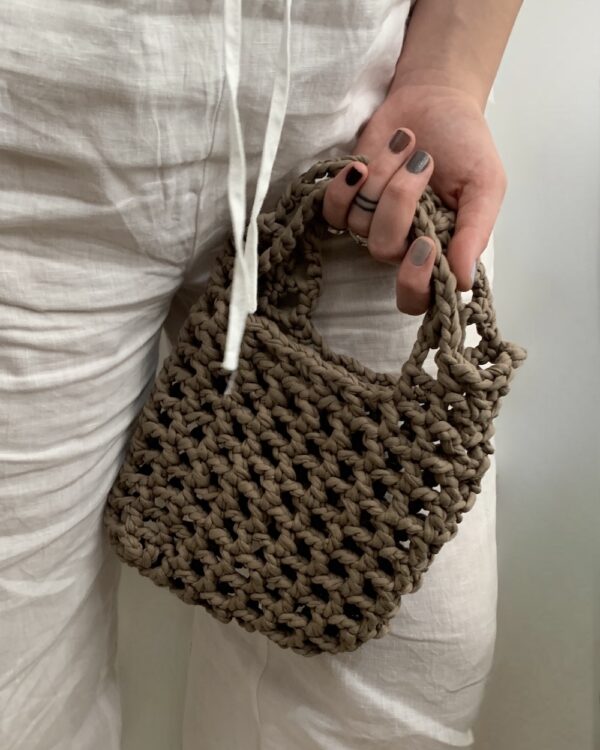 Close-up of a beautiful ash-beige crochet bag with a mesmerising mesh pattern. Perfect for a stylish and chic look.