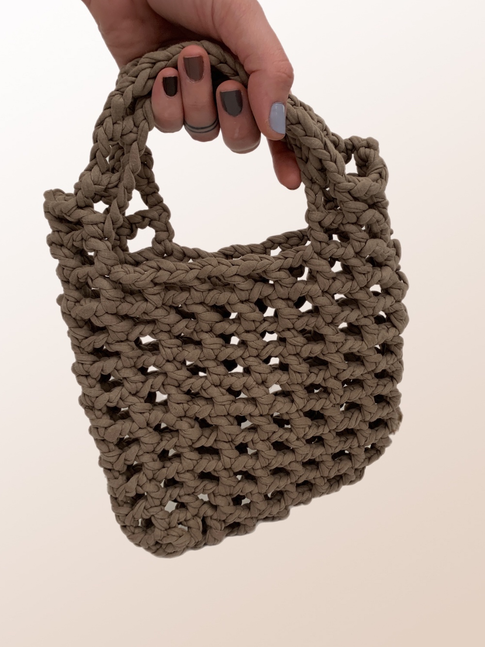 Close-up of a beautiful ash-beige crochet bag with a mesmerising mesh pattern. Perfect for a stylish and chic look.