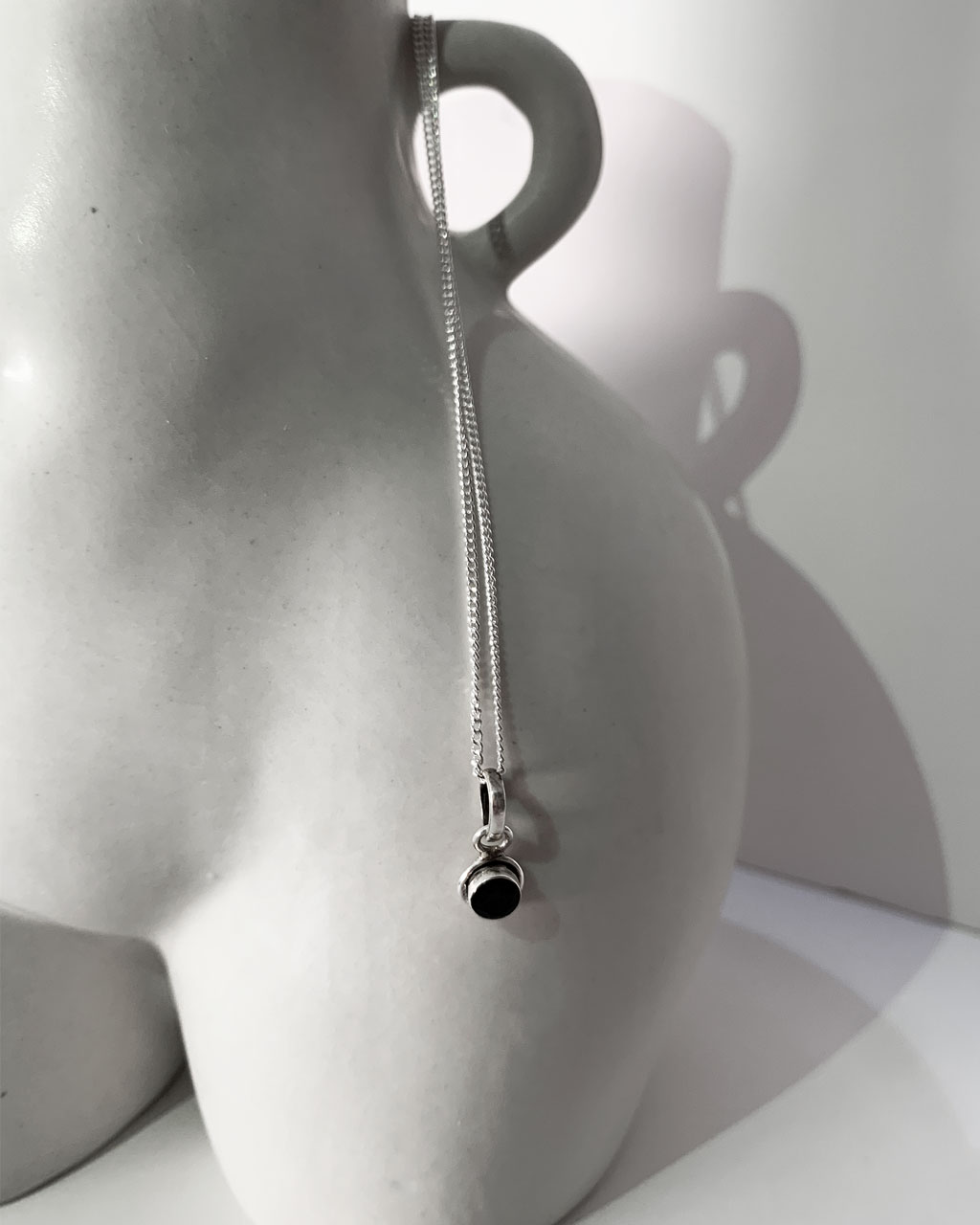 smoky topaz stone on sterling silver necklace hanging from the side of a curvy vase on a white background