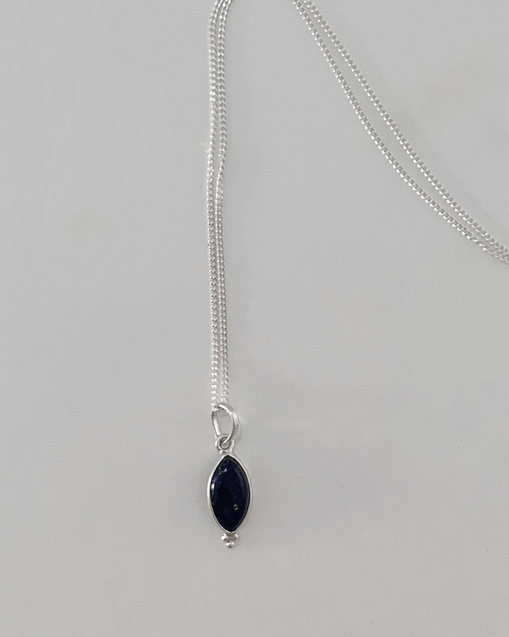 a lapis stone necklace with a sterling silver chain on a white background