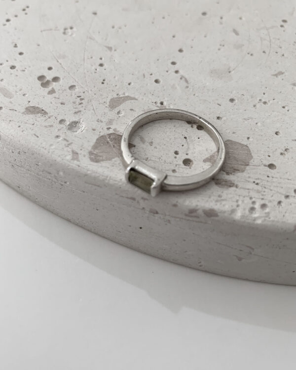 Close-up image of a shiny, sterile silver ring with a lemon topaz stone on a terrazzo tray on a white background.