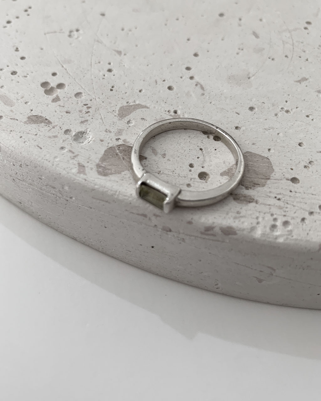Close-up image of a shiny, sterile silver ring with a lemon topaz stone on a terrazzo tray on a white background.