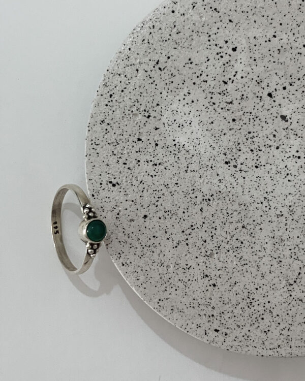 Close-up image of a shiny, sterile silver ring with a green onyx stone on a concrete coaster