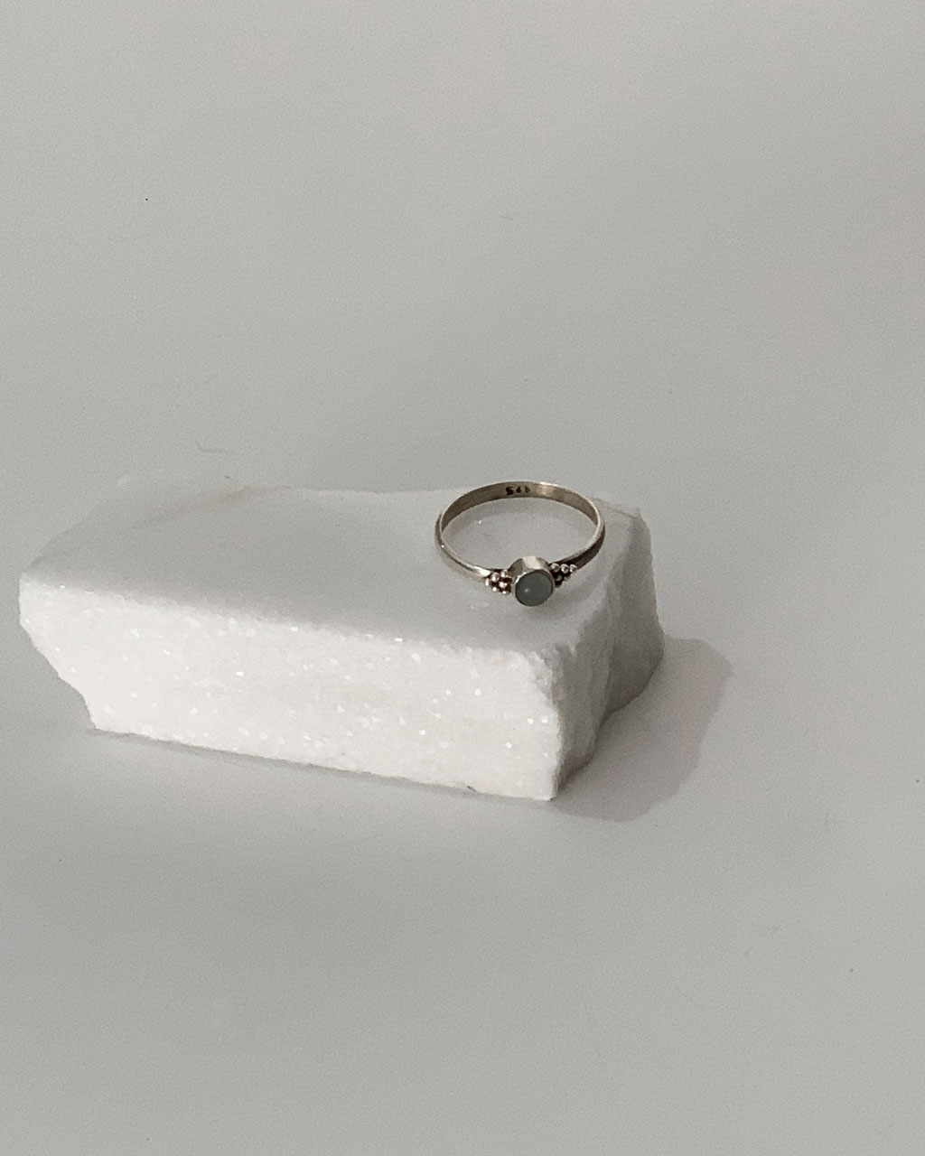 Close-up image of a shiny, sterile silver ring with a Chalcedony Aqua Stone on a white marble