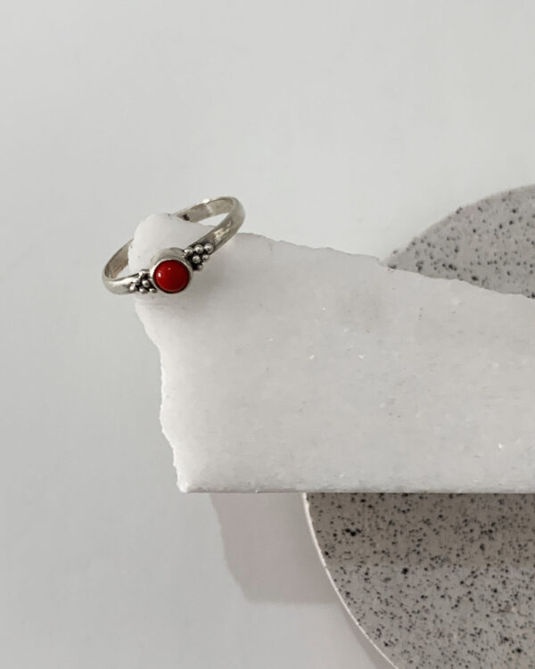 Close-up image of a shiny, sterile silver ring with a red coral stone on a white marble on a concrete coaster