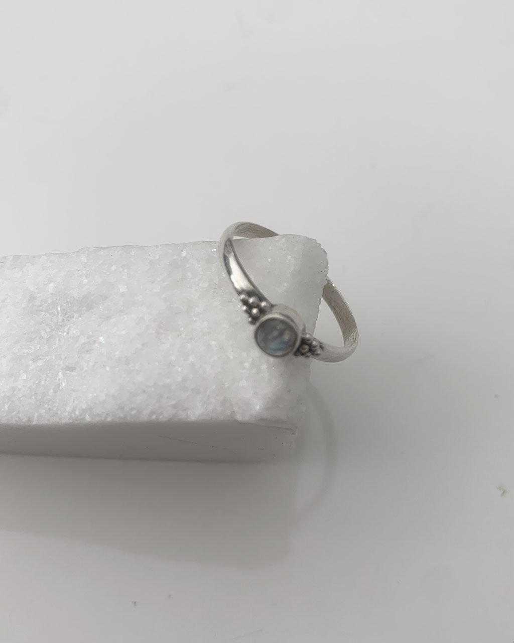 Close-up image of a shiny, sterile silver ring with a moonstone on a white marble on a white background.