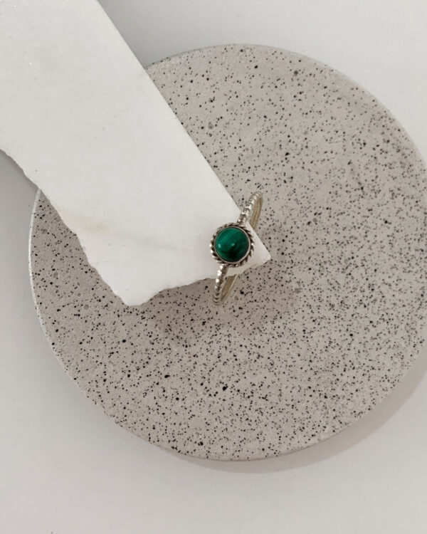 Close-up image of a shiny, sterile silver ring with a malachite Stone on a white marble on a concrete coaster