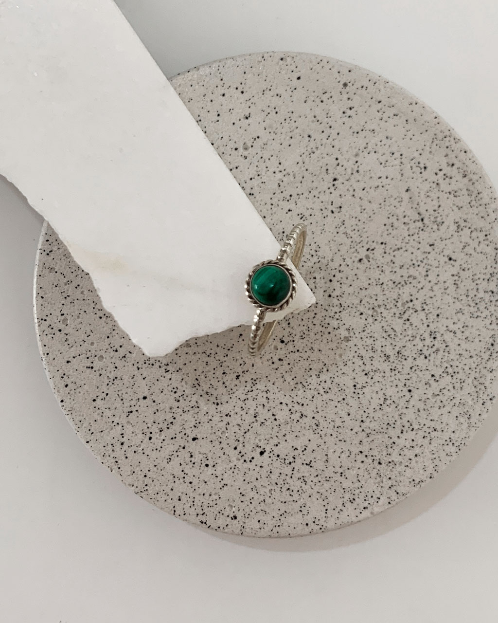 Close-up image of a shiny, sterile silver ring with a malachite Stone on a white marble on a concrete coaster