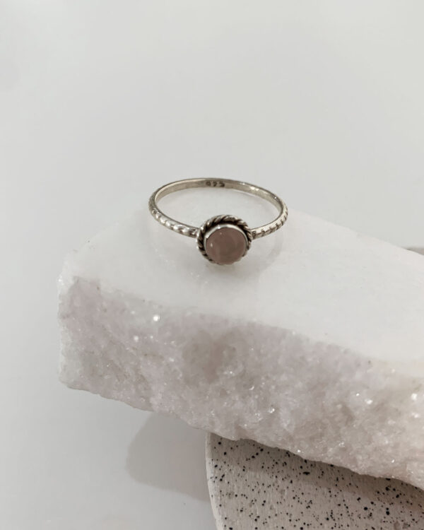 Close-up image of a shiny, sterile silver ring with a Rose quartz Stone on a white marble on a concrete coaster