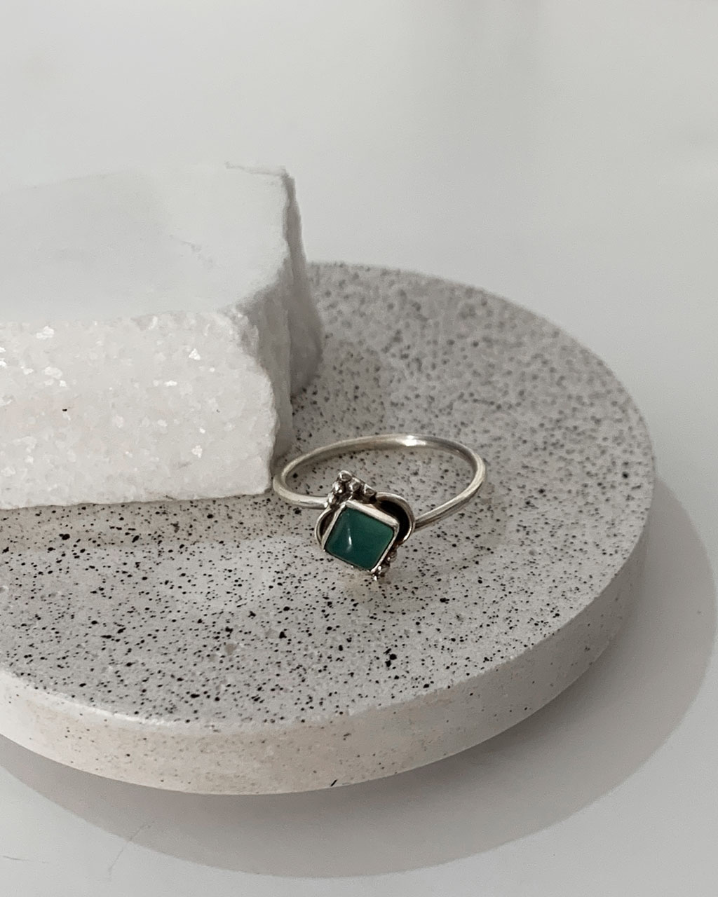 Close-up image of a shiny, sterile silver ring with a Chalcedony Aqua Stone on a concrete coaster