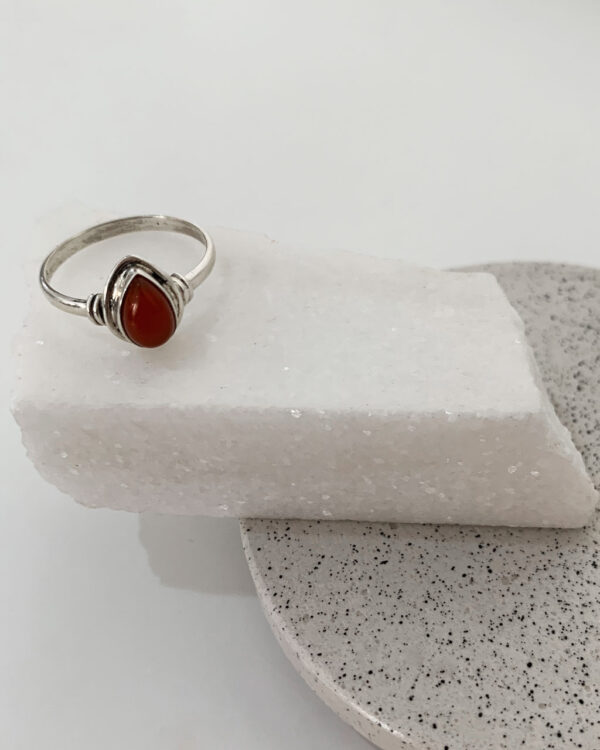 Close-up image of a shiny, sterile silver ring with a carnelian stone on a white marble on a concrete coaster