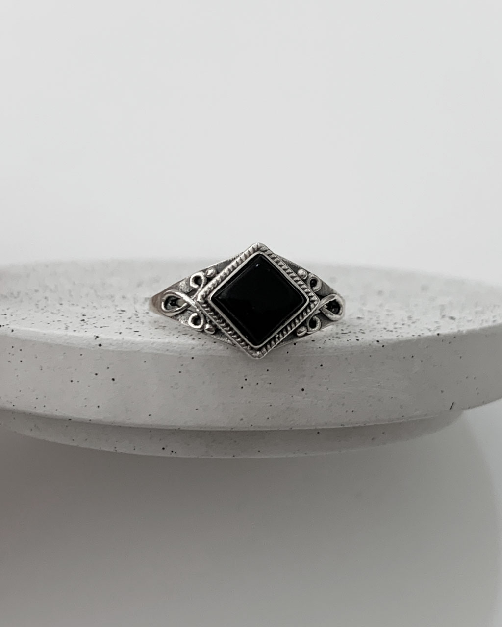 Close-up image of a shiny, sterile silver ring with a lemon topaz stone on a terrazzo tray on a white background.