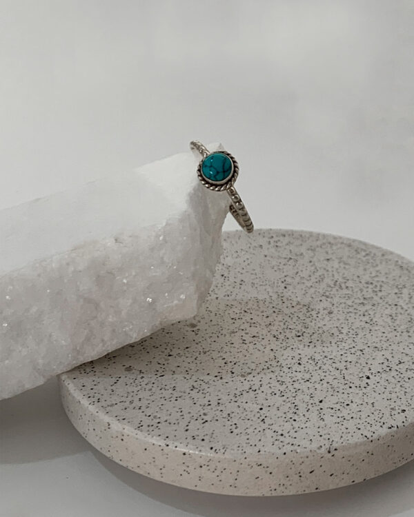 Close-up image of a shiny, sterile silver ring with a Turquoise Stone on a white marble on a concrete coaster