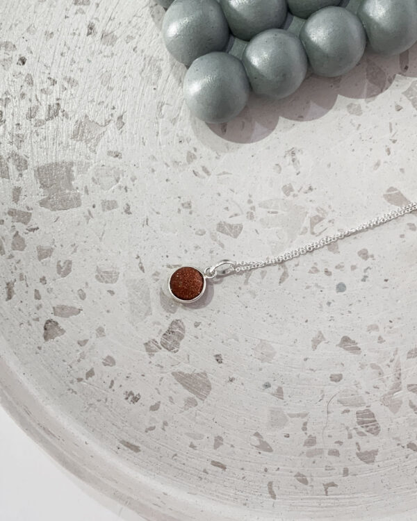 Gold sun stone necklace on a terrazzo tray
