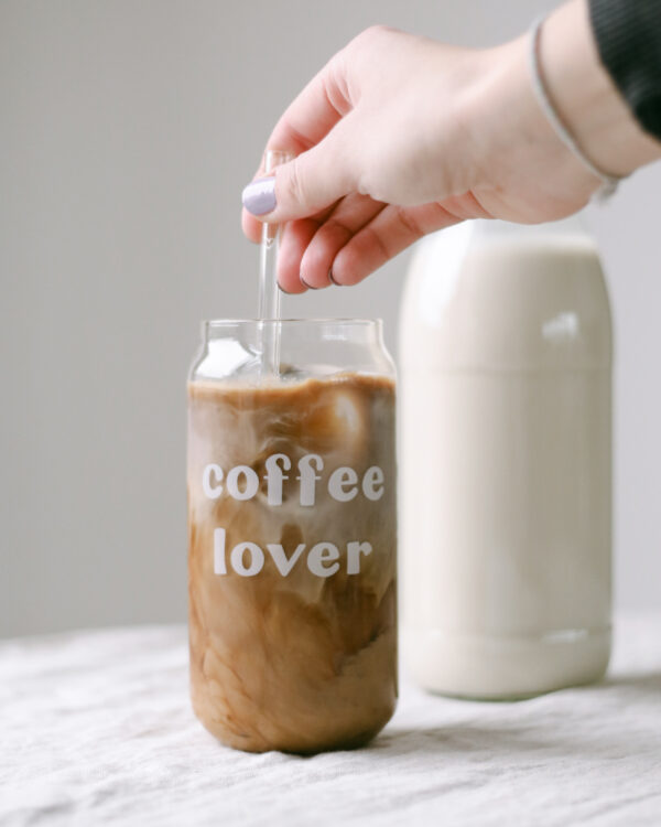 A tall drinking glass filled with dark, aromatic coffee and engraved coffee lover in white colour.